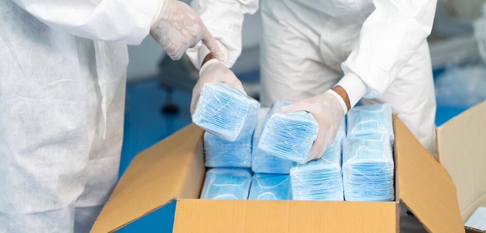 Trabajadores que usan guantes y trajes médicos empacan una caja de mascarillas.