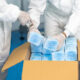 Trabajadores que usan guantes y trajes médicos empacan una caja de mascarillas.